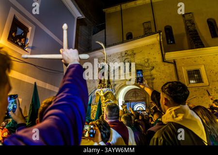 Dichte Menschenmassen versammeln sich im Dunkeln vor der Pfarrkirche von El Salvador zu Beginn der Good-Friday-Prozession Camino del Calvario. Ein Teilnehmer hält eine hölzerne Kreuznachbildung hoch, während eine Heiligenstatue auf einer vergoldeten Plattform im Hintergrund wartet. Die Turbas erzeugen hier einen rauen Lärm, der die dramatische Situation der Passion widerspiegeln soll. Die aufgebrachte Menge ruft "Kreuzige ihn". Plaza Salvador, Cuenca, Castilla-La Mancha, Spanien. Die Turbas-Tradition reicht bis zu ihrer ersten Prozession am 4. April 1616 zurück. Mitglieder, bekannt als Turbos, spielen selbstgemachte Trommeln und blasen Blechtrumpeten - die schiefen Tr Stockfoto