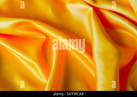 Draufsicht auf leuchtend gelbe Seide in weichen, glatten Wellen mit glänzender Oberfläche. Geeignet für Design und Hintergrundtapeten. Stockfoto