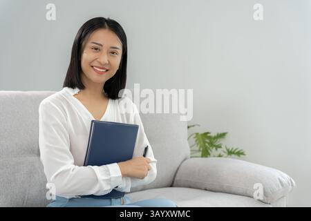 Arbeitende Frau, Porträt eines lächelnden Asienmädchens in Arbeitskleidung, im Büro sitzen und recherchieren, Kopierraum, fröhliches, nettes Geschäft, positive ENE Stockfoto