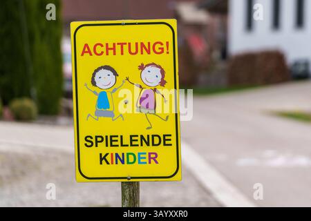 Bayern, Deutschland - 20. April 2025: Gelbes Verkehrsschild mit der Aufschrift Achtung spielende Kinder Achtung: Kinder auf Ständen am Straßenrand und warnt Autofahrer vor spielenden Kindern in der Umgebung *** ein gelbes Verkehrsschild mit der Aufschrift Achtung spielende Kinder stehen am Straßenrand und warnt Autofahrer vor spielenden Kindern in der Umgebung Stockfoto