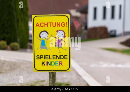 Bayern, Deutschland - 20. April 2025: Gelbes Verkehrsschild mit der Aufschrift Achtung spielende Kinder Achtung: Kinder auf Ständen am Straßenrand und warnt Autofahrer vor spielenden Kindern in der Umgebung *** ein gelbes Verkehrsschild mit der Aufschrift Achtung spielende Kinder stehen am Straßenrand und warnt Autofahrer vor spielenden Kindern in der Umgebung Stockfoto