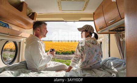 Ein Paar entspannt sich im Wohnmobil und bewundert die lebhaften Tulpenfelder von Flevoland, Niederlande. Der Frühling bringt farbenfrohe Blüten und ein Gefühl der Ruhe auf ihre Reise. Stockfoto