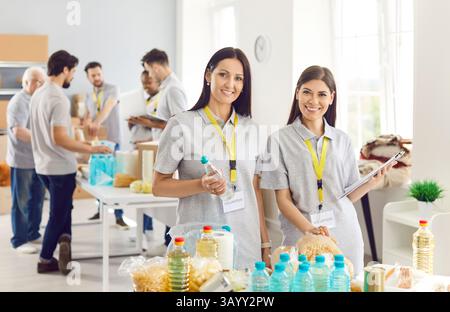 Porträt von zwei fröhlichen jungen Freiwilligen, die mit Lebensmittelgeschäft für Wohltätigkeitsessen stehen Stockfoto