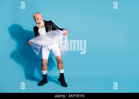 Foto in voller Länge von attraktivem extravaganten nicht-binären Kerl, der weißen Rock emtpy Raum isolierten blauen Farbhintergrund fängt Stockfoto
