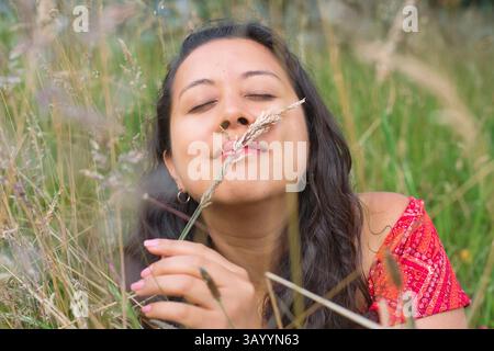 Eine Frau, die freudig die Schönheit der Natur umschließt, während sie in einem üppigen Grasfeld sitzt Stockfoto