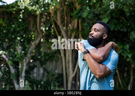 Afroamerikaner, der den Arm über die Brust im Garten zieht, mit Smartwatch, Kopierraum Stockfoto