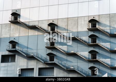 Moderne Gebäudefassade mit sich wiederholender Feuertreppe wirft rhythmischen Schatten ins Licht Stockfoto