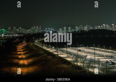Nächtlicher Blick auf eine moderne koreanische Skyline mit einem hell beleuchteten Flussweg und einer beleuchteten Brücke, die die urbane Lebendigkeit und die Infrastruktur erfasst Stockfoto