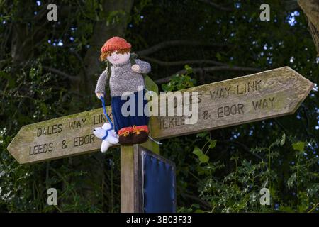 Yarnbombe Person am Fingerpfosten befestigt (öffentlicher Fernwanderweg, Ebor Way, Dales Way Link) Nahaufnahme - Menston, West Yorkshire, England Großbritannien. Stockfoto