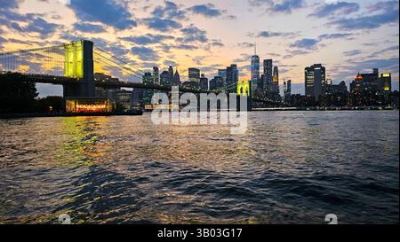 Brooklyn Bridge und New York City Skyline in der Abenddämmerung. Die berühmte Brooklyn Bridge erstreckt sich über den East River und ist vor einem lebhaften Sonnenuntergang beleuchtet Stockfoto