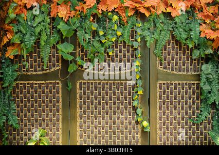 Javanische zeremonielle Hochzeitsrituale im Hintergrund mit gewebtem Rattan und Holzpaneelen, verziert mit synthetischen leuchtenden orangefarbenen Herbstblättern Stockfoto