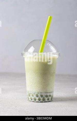 Ein Glas Eismatcha-Grüntee-Latte zum Mitnehmen mit einer Blase auf grauem Hintergrund Stockfoto