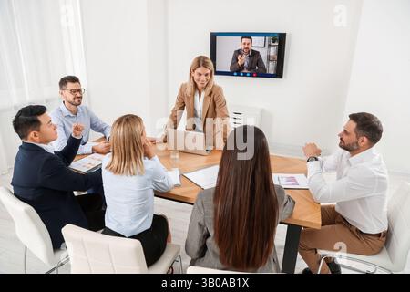 Redner, der über Online-Videochat an der Vorlesung teilnimmt. Publikum und Trainer im Konferenzraum mit Fernseher Stockfoto