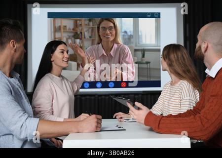 Redner, der über Online-Videochat an der Vorlesung teilnimmt. Publikum im Konferenzraum mit Projektionsleinwand Stockfoto