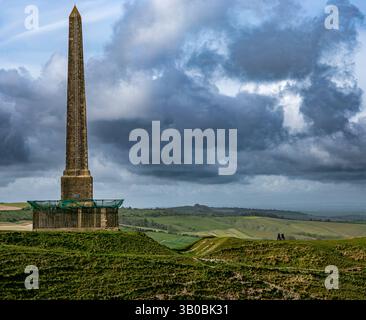 Das Lansdowne Monument steht inmitten von sanften grünen Hügeln mit dramatischen Wolken und zwei Personen in der Nähe von Cherhill Wiltshire UK Stockfoto