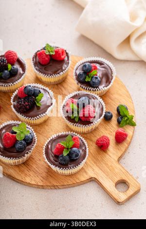 Mini-Käsekuchen in einer Muffinpfanne gebacken mit Schokoladenganache und frischen Beeren Stockfoto