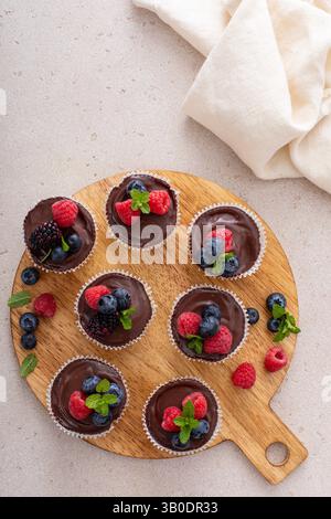 Kleine Käsekuchen in einer Muffinpfanne gebacken mit Schokoladenganache und frischen Beeren, süße Dessertidee Stockfoto