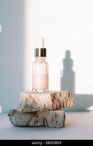 Hautpflegeserum in einer Tropfflasche auf beigen texturierten Steinen im Sonnenlicht. Stockfoto
