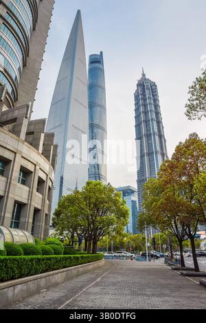 Shanghai, China - 1. April 2025: Shanghai Tower, Jinmao Tower und SWFC leuchten am Abendhimmel, eingerahmt von üppigem Frühlingslaub und ruhigen Gehwegen Stockfoto