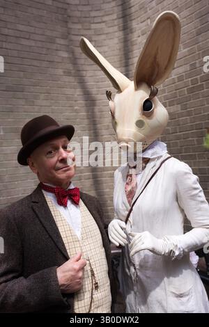 Ein Mann in Tweed-Anzug und Bowler-Hut steht neben einer Person, die eine große Kaninchenmaske und ein weißes Kleid im viktorianischen Stil trägt. Die Einstellung scheint ou zu sein Stockfoto