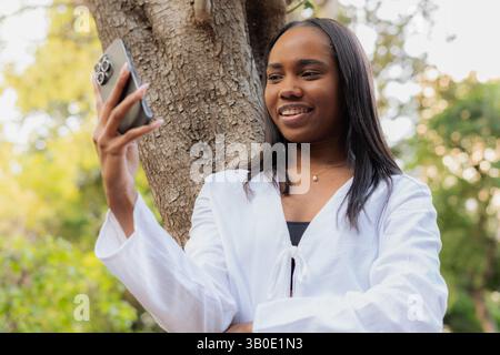 Eine junge Frau in einem weißen Labormantel, die ein fröhliches Selfie im Freien macht Stockfoto