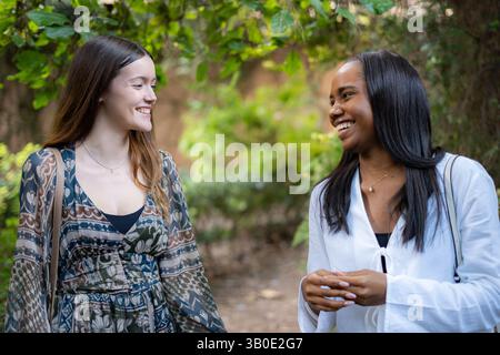 Zwei Freundinnen lachen und genießen ein lebhaftes Gespräch in einem sonnendurchfluteten Park, teilen fröhliche Momente und schaffen bleibende Erinnerungen in der Umgebung Stockfoto