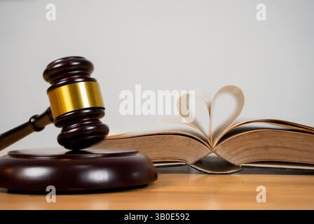 Hammer, gesetzlicher Code. Ein romantisches und sentimentales Bild mit einem offenen Buch, dessen Seiten zu einem Herzen geformt sind. Rechtskonzept, Studioaufnahmen. Hammer mit Gehörschutz Stockfoto