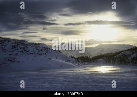 Blick auf schneebedeckte Berge und einen gefrorenen Fjord bei einem dramatischen Sonnenaufgang, Norwegen, Europa Stockfoto