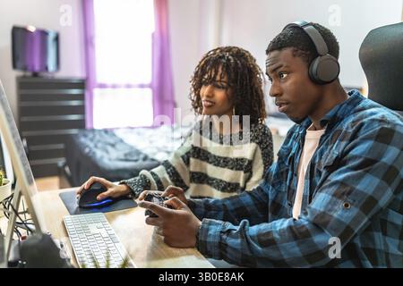 Junge Männer und Frauen genießen ihre gemeinsame Zeit, spielen Videospiele auf einem Computer und Gamepad, während sie sich zu Hause entspannen Stockfoto