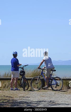 Ein Paar mittleren Alters ruht ihre Fahrräder aus und genießt den Sommertag im Ruby Bay Picknick-Bereich in der Nähe von Nelson auf der Südinsel Stockfoto