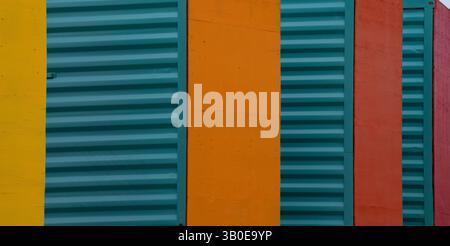 Nahaufnahme der Seiten von Versandbehältern, rot-türkisgelb-orange lackiert, stehend am Ende, mit glatter roter Seite und grüner gewellter Metallseite Stockfoto