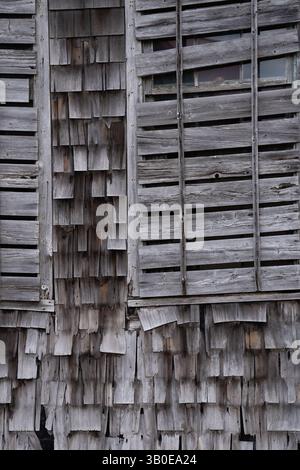 Schließen Sie die senkrechte Schwarzweiß-Linie des verschlossenen Fensters des alten Gebäudes mit Holzschindeln oder Schütteln, die verwittert und vertikal abfallen Stockfoto