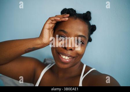 Porträt einer Afroamerikanerin, die lächelt, mit der Hand auf dem Kopf. Sie trägt ein weißes Tanktop und hat einen freundlichen, zugänglichen Ausdruck Stockfoto