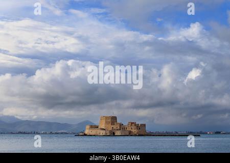 Burg Bourtzi in Nafplio, Griechenland, umgeben von Meer und Bergen unter einem stimmungsvollen Himmel mit Wolken und sanftem Licht. Stockfoto