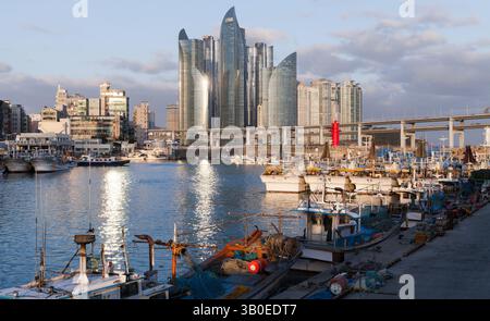 Busan, Südkorea - 16. März 2018: Eine lebhafte Hafenszene mit Fischerbooten vor dem Hintergrund einer zeitgenössischen Skyline und einer dra Stockfoto