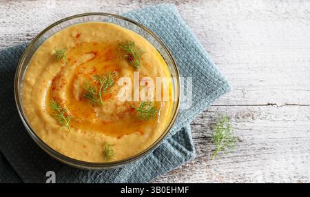 Köstlicher Hummus mit Paprika in einer Glasschale auf hölzernem Hintergrund. Gesunde und vegetarische Lebensmittel. Direkt darüber. Stockfoto