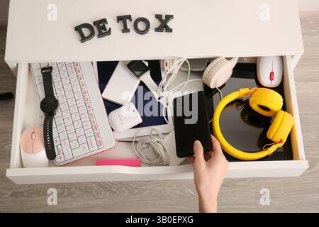Frau, die ein modernes Handy in eine offene Schublade mit verschiedenen Gadgets steckt Stockfoto