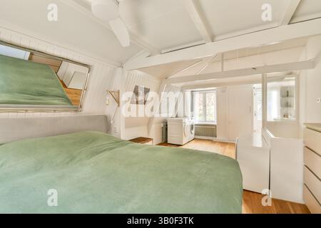 Ein helles, modernes Schlafzimmer mit einem weichen grünen Bettüberwurf, Holzfußboden und modernen Möbeln schafft eine einladende und stilvolle Atmosphäre. Stockfoto