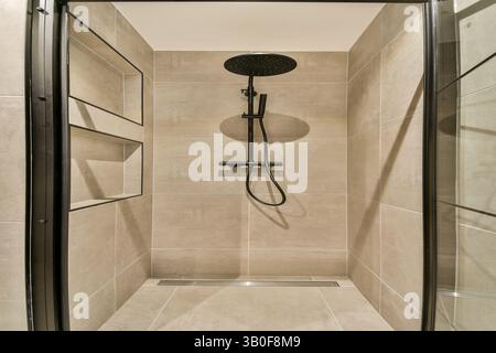 Eine moderne Duschkabine mit schlanken Linien und einem Regenduschkopf in einem stilvollen, gefliesten Raum, der minimalistisch und funktionell betont. Stockfoto