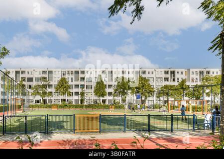 Ein lebendiger Gemeinschaftsspielplatz bietet Schaukeln und Spielbereiche inmitten moderner Gebäude und Bäume unter hellem Himmel, die einen aktiven urbanen Lebensstil zeigen. Stockfoto