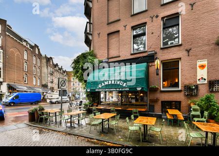 Ein gemütliches Straßencafé mit Holztischen und grünen Stühlen, umgeben von eleganten Backsteinhäusern unter einem bewölkten Himmel. Ideal zum Essen und Entspannen im Freien. Stockfoto