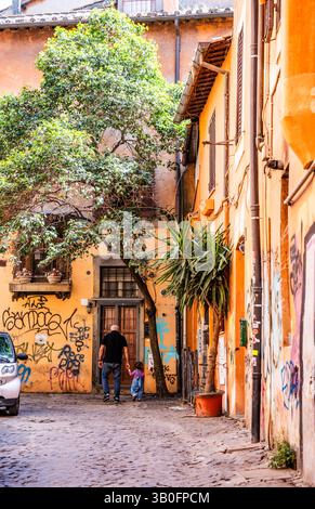 Blick auf eine ruhige Gasse mit Efeu-bedeckten Wohnhäusern und üppiger Vegetation, Opa und Neffe im Viertel Trastevere in Rom, Italien. Stockfoto