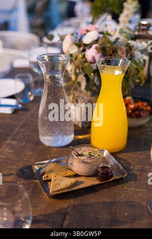 Holztisch bei einem Bankett mit Karaffen mit frischem Wasser und Orangensaft, Blumen und Hors d'oeuvres. Stockfoto