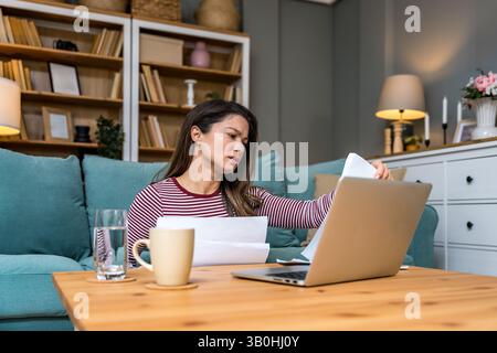 Finanzkrise. Eine junge besorgte Geschäftsfrau, die zu Hause sitzt und versucht, einen Ausweg zu finden und das Einkommen und die Ausgaben ihrer kleinen, globalen Gesellschaft zu berechnen Stockfoto
