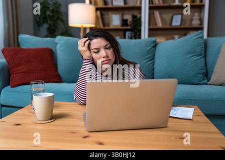 Finanzkrise. Eine junge besorgte Geschäftsfrau, die zu Hause sitzt und versucht, einen Ausweg zu finden und das Einkommen und die Ausgaben ihrer kleinen, globalen Gesellschaft zu berechnen Stockfoto