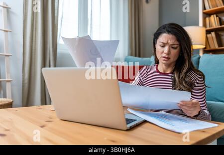 Finanzkrise. Eine junge besorgte Geschäftsfrau, die zu Hause sitzt und versucht, einen Ausweg zu finden und das Einkommen und die Ausgaben ihrer kleinen, globalen Gesellschaft zu berechnen Stockfoto