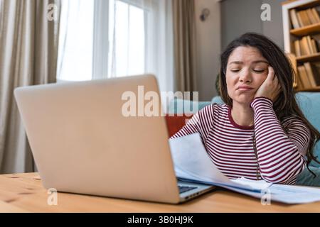Finanzkrise. Eine junge besorgte Geschäftsfrau, die zu Hause sitzt und versucht, einen Ausweg zu finden und das Einkommen und die Ausgaben ihrer kleinen, globalen Gesellschaft zu berechnen Stockfoto