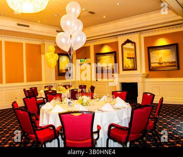 Eleganter Bankettsaal mit runden Tischen, roten Stühlen, weißen Tischdecken und Ballondekorationen. Stockfoto
