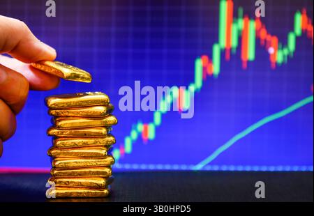 Nahaufnahme der Fotohand mit einem Goldbarren auf der Kerzenkarte. Hintergrund , Schwankungen der Goldpreise Konzept. Stockfoto