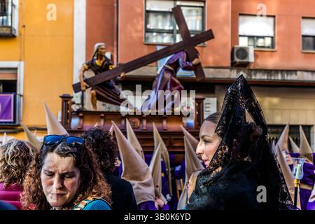 Der Hermandad de Nuestro Padre Jesús Caído y La Verónica trägt den gleichnamigen paso. Es zeigt die Szene, in der Jesus auf dem Weg zur Kreuzigung unter dem Gewicht des Kreuzes zusammenbricht und die hl. Veronika ihm den Schweißstoff überreicht. Die trauernden Frauen mit Schleiern und Mantilla (Manolas) zeigen die Verbindung zwischen biblischen Ereignissen und dem modernen Leben: Sie drücken das Mitgefühl und die Sympathie der Gemeinschaft aus und schaffen eine Brücke zwischen religiöser Tradition und der persönlichen Erfahrung von Trauer und Hoffnung. Calle las Torres, Cuenca, Castilla-La Mancha, Spanien Stockfoto